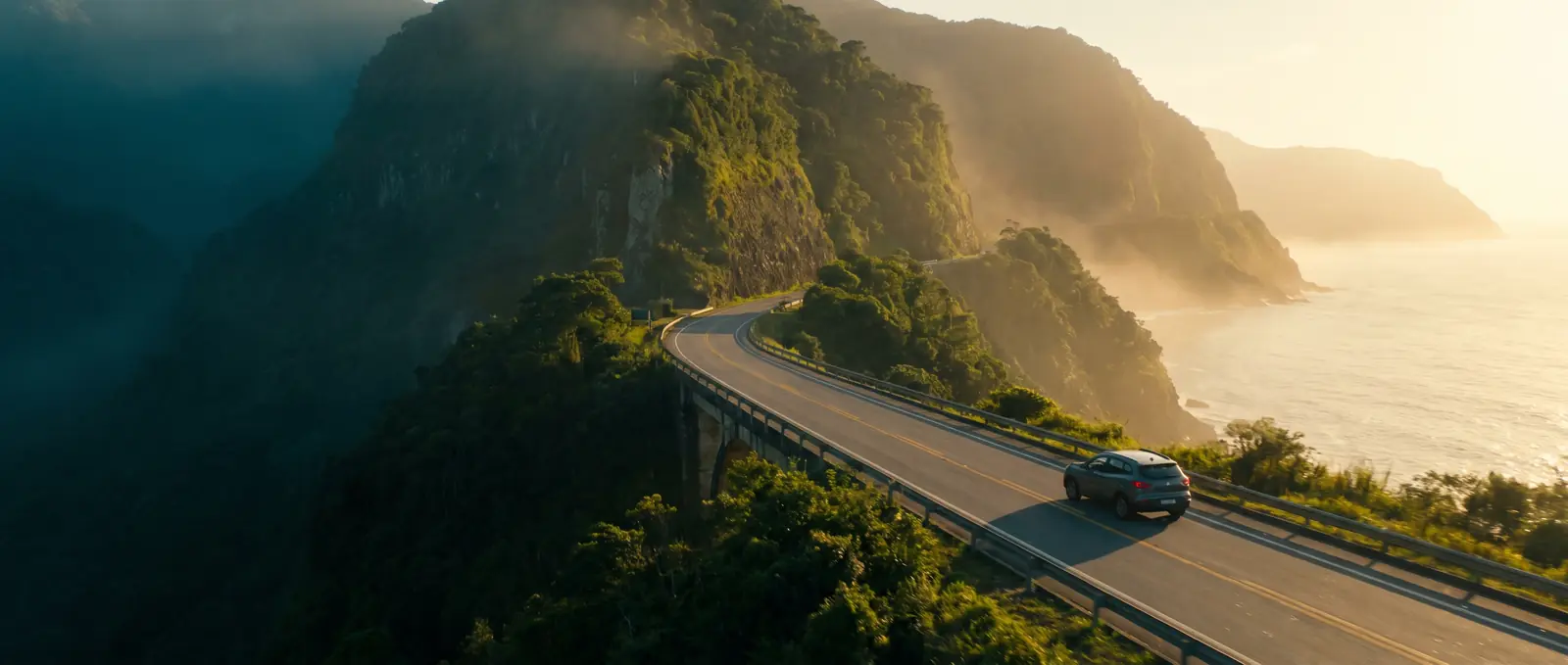Estrada litorânea brasileira no fim da tarde, com o mar à esquerda e a serra à direita
